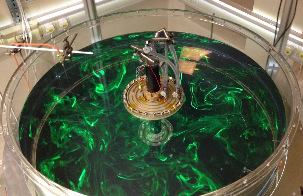 <strong>Figure 1.</strong> A one-meter-diameter rotating cylindrical tank containing a water-glycerol mixture with tracer particles appearing in green. The water is heated by a ring at the bottom of the tank, and cooled by the disk at the top. The turbulent eddies exhibit the same wavelength scaling as observed high in Earth’s atmosphere. Photo courtesy of H. Scolan of Claude Bernard University Lyon 1. 