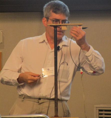 Jared Bronski adjusts his table-top ring dropper to demonstrate the mathematical concepts of the classic magic trick involving a ball chain and steel ring.