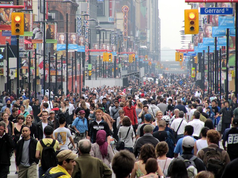 Crowds in Yonge Street, Toronto. Collective crowd behavior emerges from individual interactions at the local level. Image credit: Wikimedia Commons.